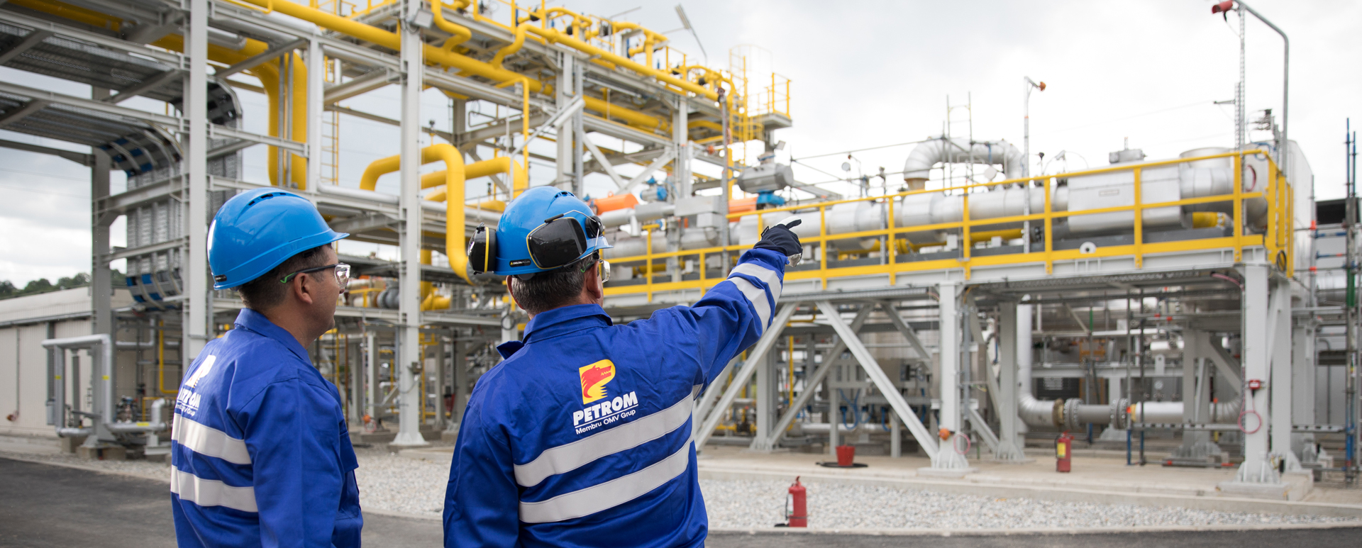 Neptun Deep announced to be developed by OMV Petrom and ROMGAZ, image shows two workers in blue uniforms and helmets with the OMV Petrom logo on, pointing at a yellow oil rig