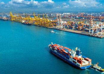 Arinto provides 'arrival optimisation' tech for more efficient sea voyages, MTB Events, image shows cargo vessel ariving at a port filled with other colourful ships, the sea is a deep blue