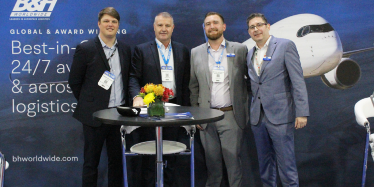 AerFin Ltd appoints B&H Worldwide to manage inventory in Singapore and Australia., MTB Events, Image shows members of Aerfin & B&H standing alongside eachother behind a black table with flowers on top. In the background there is a large image of a plane.