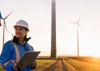 RWE wins tender for 30MW wind farm in Hessian, MTB Events, Image shows a man and woman looking at a clipboard at a wind farm at sunset, both persons are in blue safety jackets and helmets