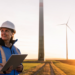RWE wins tender for 30MW wind farm in Hessian, MTB Events, Image shows a man and woman looking at a clipboard at a wind farm at sunset, both persons are in blue safety jackets and helmets