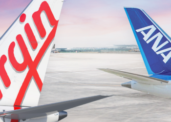 Expanded partnership between Virgin Australia & ANA offers even more benefits for passengers, MTB Events. Image shows two tails of two planes, one with the text 'Virgin' in red like the logo, the other is blue with 'ANA' in white text. Both are on tarmac at sunrise.