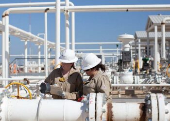 Worley recognised and awarded as winner in the Sustainability Leaders List, MTB Events. Image shows two women in white hard harts looking at a notepad and white hydrocarbon pipes, more hydrocarbon pipes are in the background