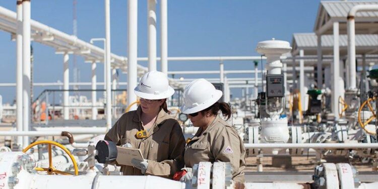 Worley recognised and awarded as winner in the Sustainability Leaders List, MTB Events. Image shows two women in white hard harts looking at a notepad and white hydrocarbon pipes, more hydrocarbon pipes are in the background