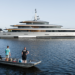 Feadship's Obsidian sets a higher standard for carbon reduction, MTB Events, image shows the superyacht, 'Obsidian', in the ocean with two men standing on a small boat looking at the yacht