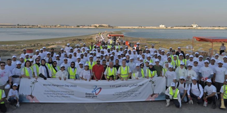Bapco Energies continues their modernisation project with mangrove plantation & beach clean up, MTB Events. Image shows participants of the clean up on the Ma'ameer shore holding a large sign with the title 'World Mangrove Day 2023'.