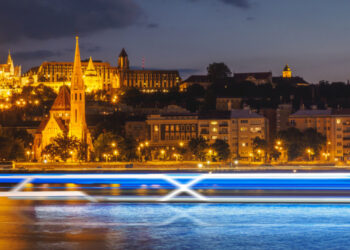Celebrity Cruises unveils exciting new venture: Celebrity River Cruises, MTB Events. Image shows a time lapse of a cruise sailing across a river at night in front of lit up buildings and a castle in the background.