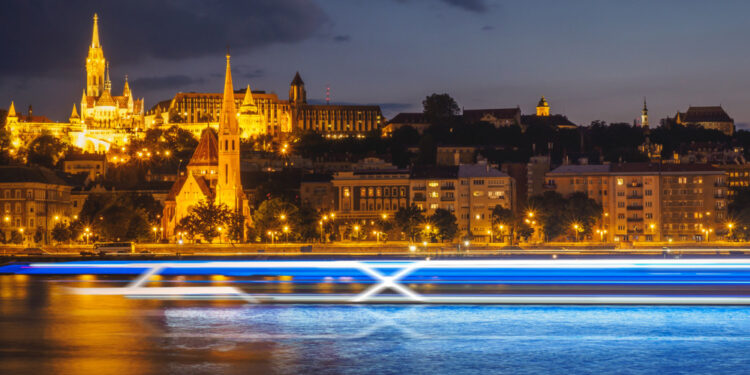 Celebrity Cruises unveils exciting new venture: Celebrity River Cruises, MTB Events. Image shows a time lapse of a cruise sailing across a river at night in front of lit up buildings and a castle in the background.