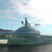 Image shows the concept art of the superyacht called Project DROP, the yacht is green in colour with a large glass dome on top, it is shown on the sea with mountains in the background. Allstars Design redefines luxury with the unveiling of Project DROP, MTB Events.