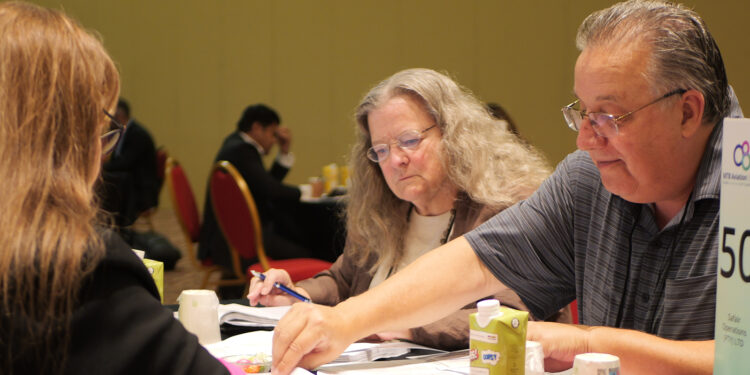 Image shows a man and a woman side on towards the camera pointing at a document on a table, with another woman in the foreground. From Meetings to Memories: Reflecting on MTB Aviation Europe 2025, MTB Events.