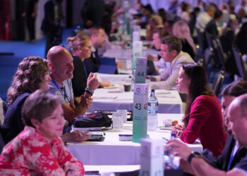Image shows white tables going vertically along a hall with people sat either side in a room lit with blue and pink lights. Connections, Collaboration and Community was the theme of this year’s MTB Marine Europe , MTB Events.