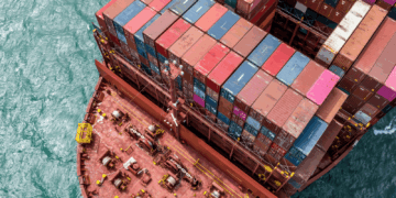 Image shows a top down view of the front side of a red container ship with colourful containers stacked up. Signal Ocean Expands Maritime Intelligence Offering Through AXSMarine Acquisition, MTB Events.
