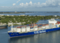 Image shows a container vessel with the text 'TOTE Maritime' down the side. Two Tugboats are in front and behind the vessel. New LNG Bunkering Agreement Supports U.S. Maritime Fuel Transition, MTB Events.