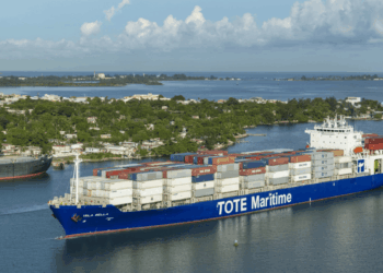 Image shows a container vessel with the text 'TOTE Maritime' down the side. Two Tugboats are in front and behind the vessel. New LNG Bunkering Agreement Supports U.S. Maritime Fuel Transition, MTB Events.