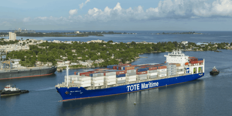 Image shows a container vessel with the text 'TOTE Maritime' down the side. Two Tugboats are in front and behind the vessel. New LNG Bunkering Agreement Supports U.S. Maritime Fuel Transition, MTB Events.