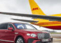 Image shows a red Bentley motor car in the foreground and a yellow and red DHL airfreight airplane in the background, both on a runway. Bentley Motors Transitions to SAF Across Worldwide Air Shipments, MTB Events.