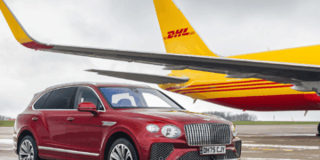 Image shows a red Bentley motor car in the foreground and a yellow and red DHL airfreight airplane in the background, both on a runway. Bentley Motors Transitions to SAF Across Worldwide Air Shipments, MTB Events.