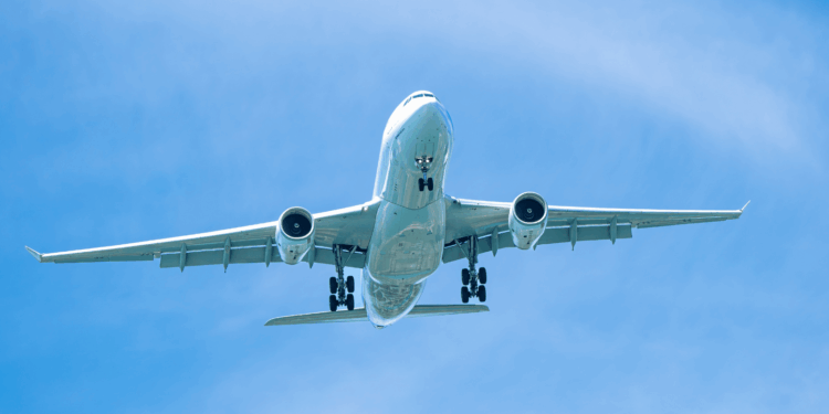 Image shows an aircraft from below as it flies in a blue sky with thin clouds. Engineers Develop Solar-Driven Process for Next-Generation Aviation Fuel, MTB Events.